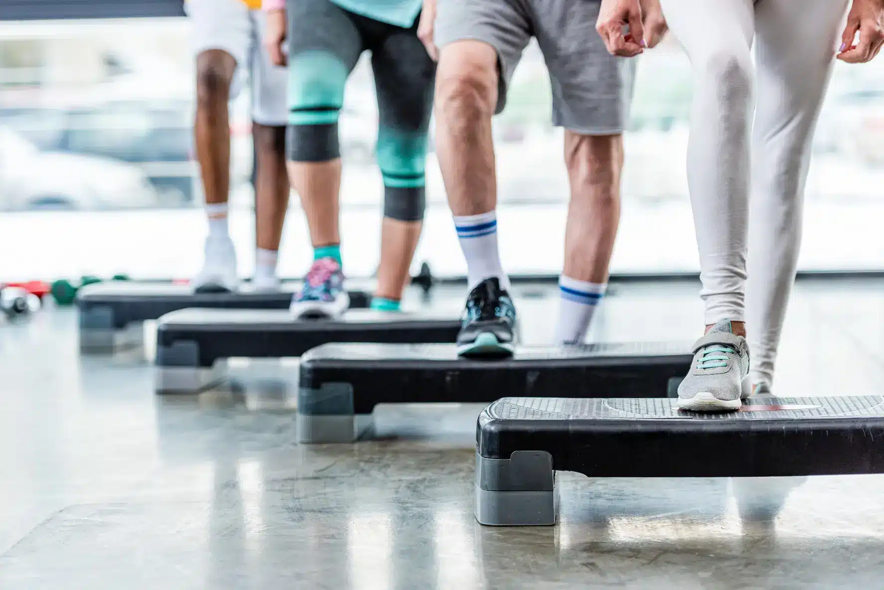 Groupe de personnes en vêtements de sport faisant de l'aérobic ou de la musculation avec des step en salle de sport, vues des jambes.