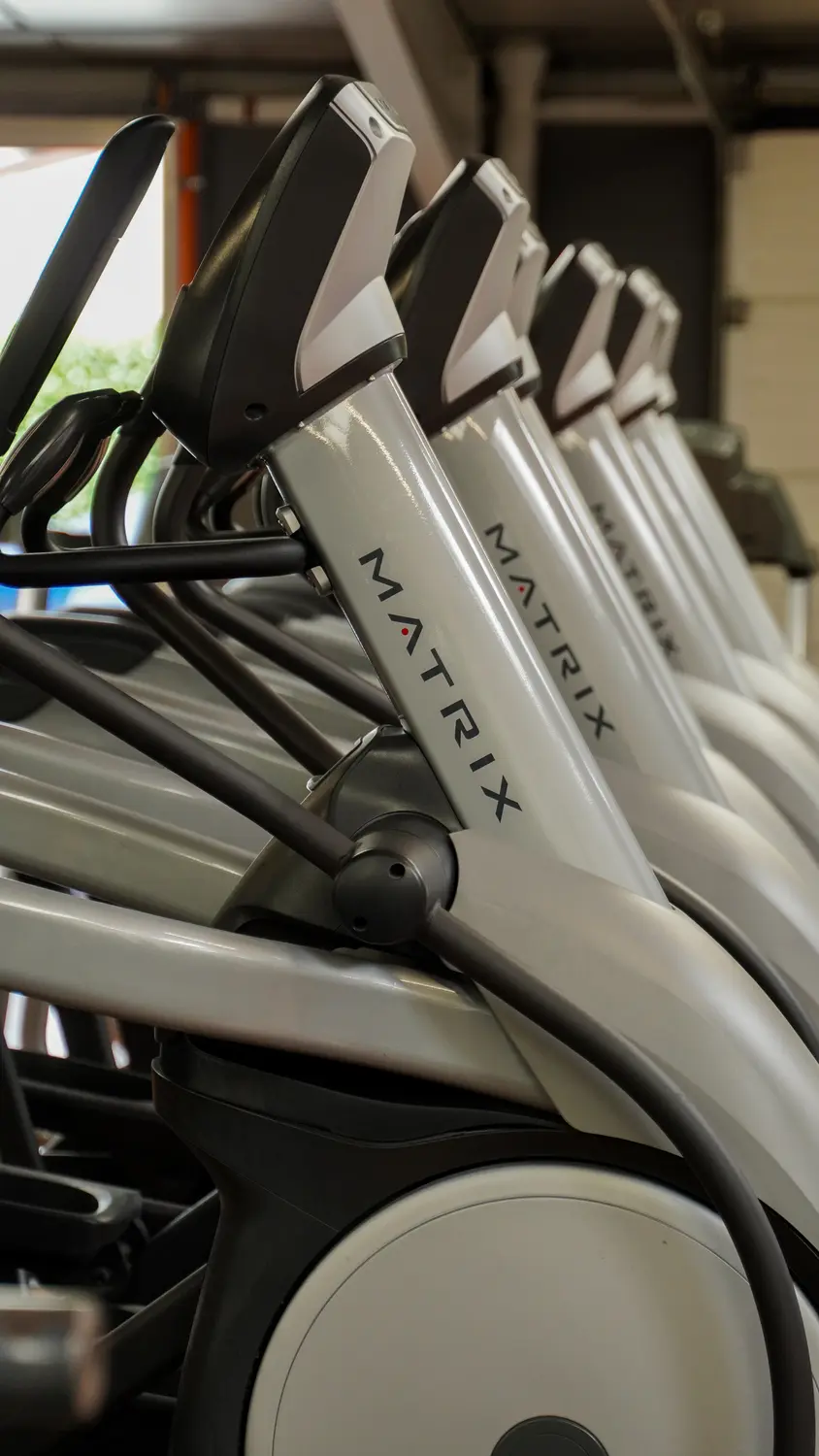 Rangée d'équipements de fitness Matrix elliptiques gris et noirs, alignés dans une salle de sport. Le logo MATRIX est visible.
