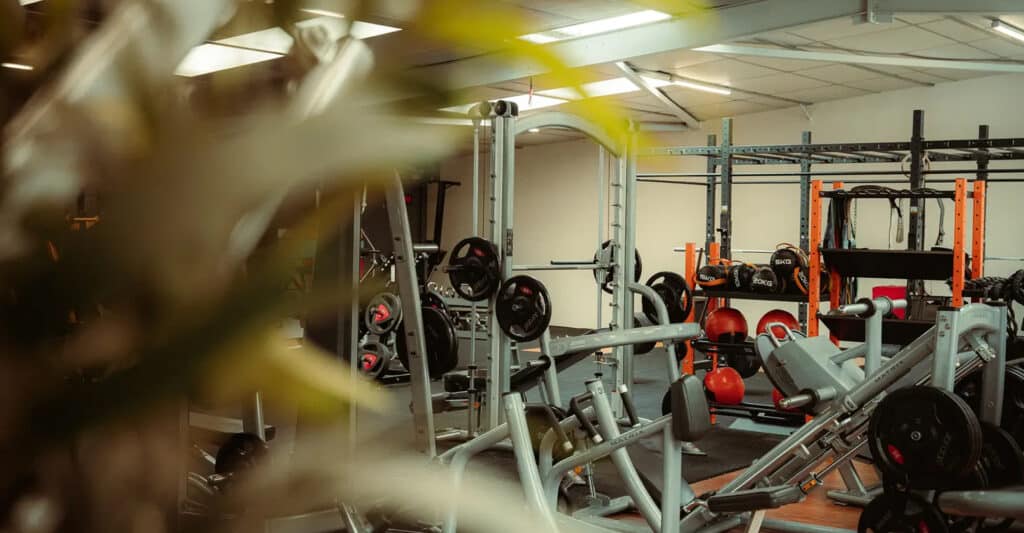 Intérieur d'une salle de sport moderne avec équipement de musculation, incluant une machine Smith, un presse à cuisses Matrix, des haltères et des plaques de poids Jordan (20KG).