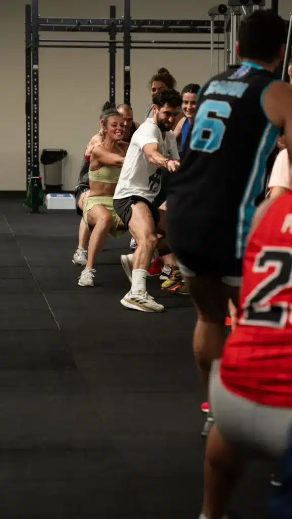 Tir à la Corde Intense : Entraînement de Force en Groupe Groupe déterminé en plein tir à la corde dans une salle de sport, une femme en brassière jaune et un homme en t-shirt blanc en pleine traction.