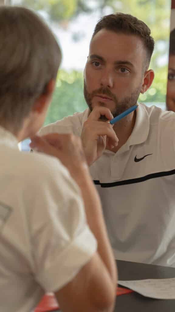 Consultation professionnelle : homme en réflexion sérieuse Gros plan d'un homme attentif en polo blanc (Nike) tenant un stylo bleu sur le menton, écoutant l'interlocuteur lors d'une consultation.